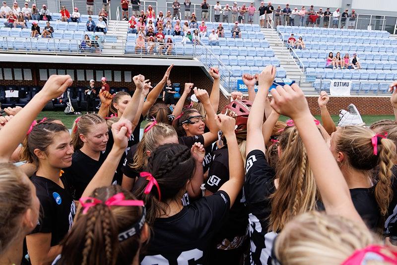 group of women athletes in huddle with arms raised